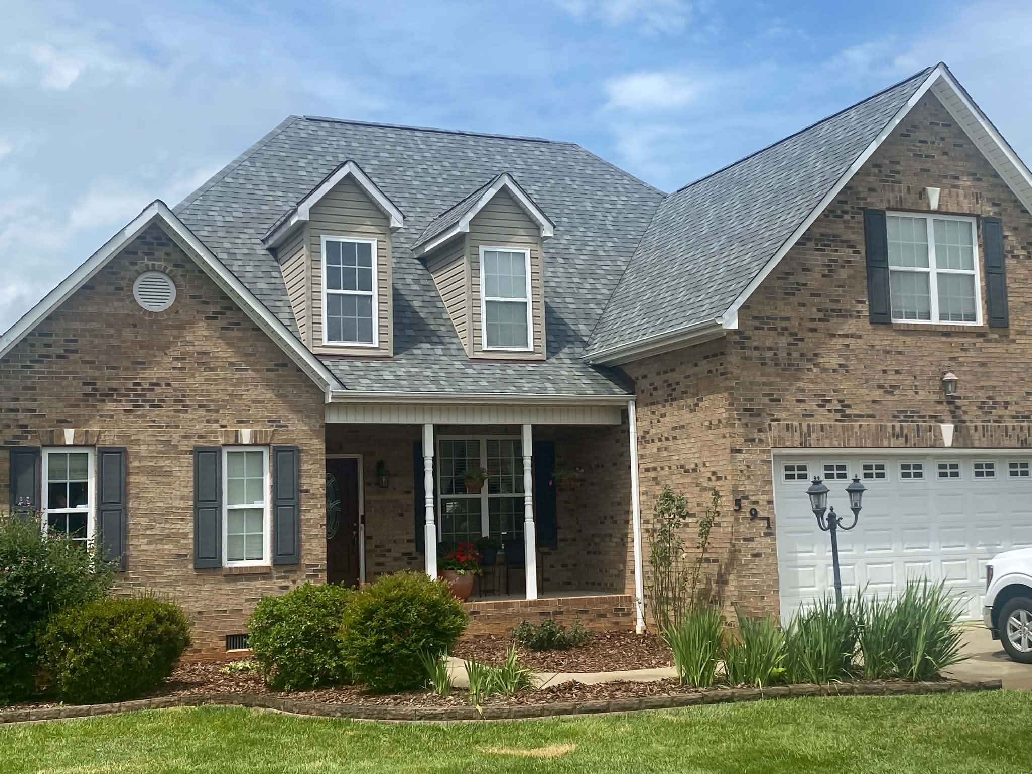 Front view of a completed gray shingle roof on a brick home